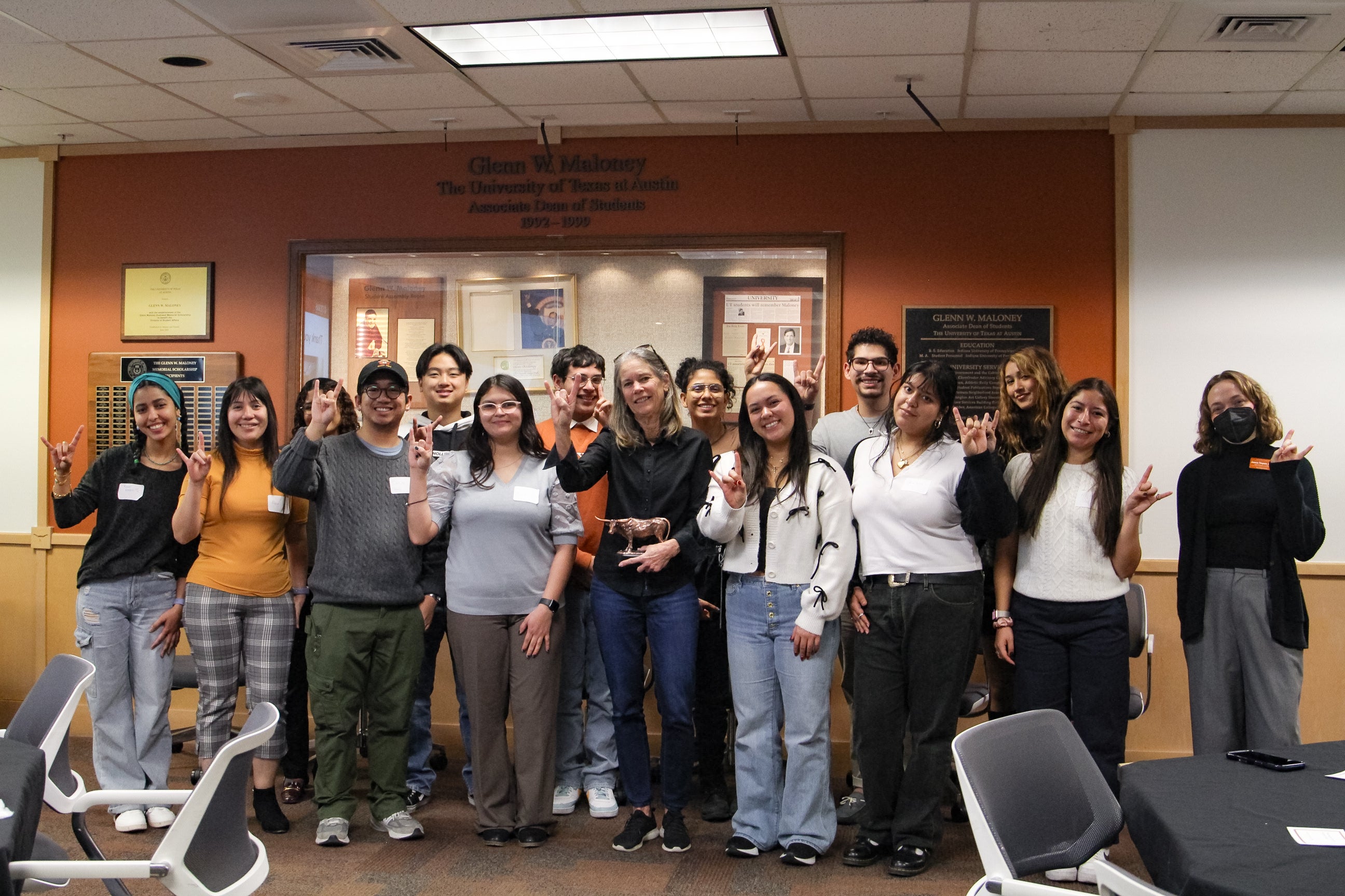 large group of students standing together with the founder of HHH. The students and the founder are holding up a Hookem Horns Handsign. The founder is holding a metal-plated longhorn figure.