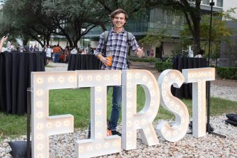 Male student poses with FIRST marquee at the First-Gen Celebration