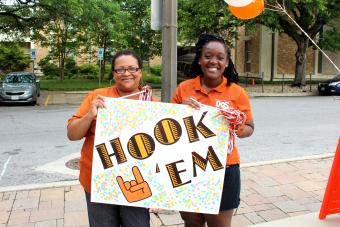 staff member and student holding a "Hook 'Em" sign