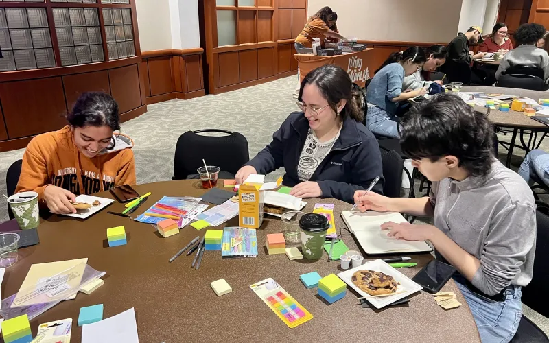 three students sitting at a round table with planner decorating supplies like stickers, pens and colorful paper. 