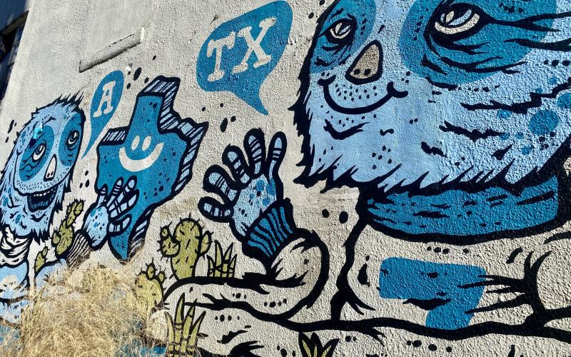 Wall Art of a blue creature saying "TX" and another creature saying "A" to spell ATX. A blue Texas is painted in between them.